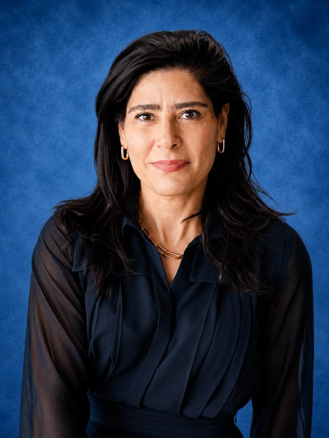 Professional woman in dark blouse with a blue background.