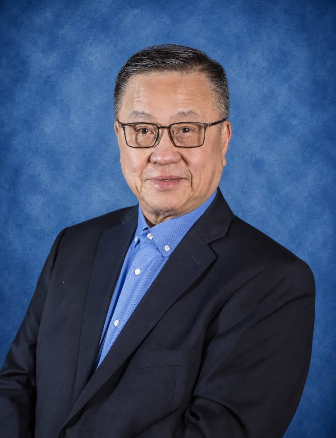 Professional portrait of a senior male executive in a suit and glasses.