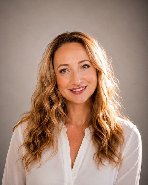 Professional portrait of a smiling woman with long wavy auburn hair in a white blouse, studio background.